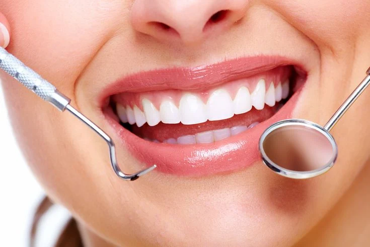 Close-up of a woman's smiling teeth with a dental mirror and explorer tool held near her mouth